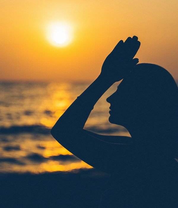 Woman in a calming yoga pose in a dimly lit room, suggesting evening practice.